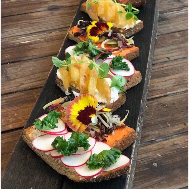 Serving board with a variety of small tartness garnished in colorful vegetables slices and a sprinkle of microgreens